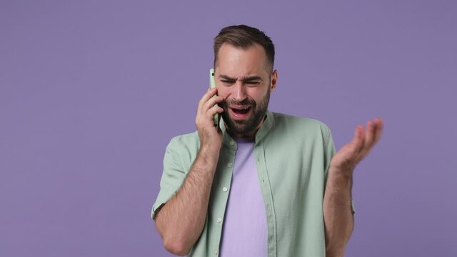 Perplexed angry displeased nervous young bearded man 20s years old wears mint shirt talk on mobile cell phone ask what bad news scream swear isolated on plain light purple background studio portrait