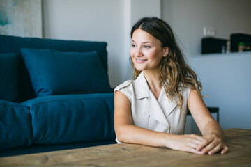 Smiling thoughtful woman with brown hair sitting at table in living room