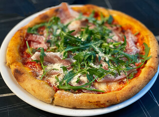 Close-up on a restaurant table pizza with prosciutto, arugula and parmesan cheese