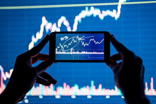 Businesswoman holding mobile phone with stock market data in office