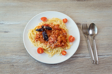 Spaghetti in a white plate with bacon and bolognese sauce on the background of a light wooden table. Family lunch, Italian dish.