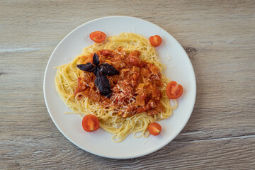 Spaghetti in a white plate with bacon and bolognese sauce on the background of a light wooden table. Family lunch, Italian dish.