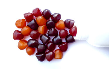 Group of red, orange and purple multivitamin gummies with the bottle isolated on white background. 
