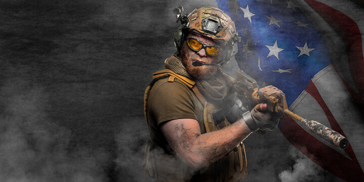 Professional special forces soldier, during a special operation in smoke against a dark concrete wall and US flag background - he is defending flag. Photo with copy space - format 2x1.