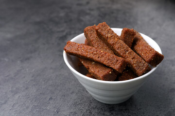 Crispy rusks in bowl on grey table, closeup