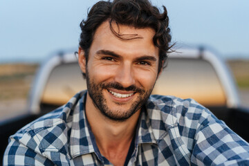 Young white man smiling at camera while sitting in trunk