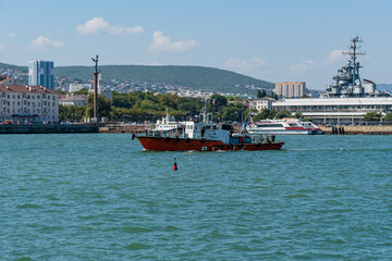 Ttug "Kapitan Fofonov" is sailing along bay. In background - building of Marine Station and Admiral Serebryakov Embankment. Pedestrian recreation area. Novorossiysk, Russia - September 15, 2021