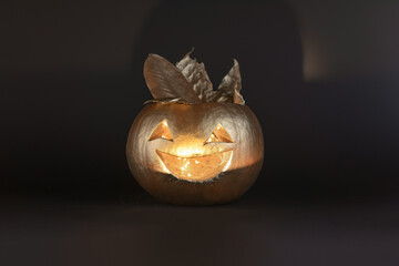 Carved scary smiling pumpkin in gold color on a black background. The concept of Halloween decorations.