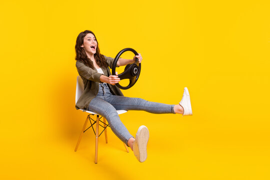 Portrait of nice funny cheerful girl sitting on chair holding steering wheel riding fooling isolated over bright yellow color background