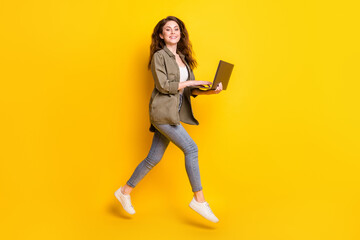 Full length body size view of attractive cheerful girl jumping using laptop isolated over bright yellow color background