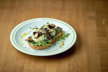 Avocado toast with mushrooms and poached egg in a white plate on a wooden background