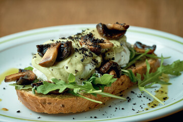Avocado toast with mushrooms and poached egg in a white plate on a wooden background