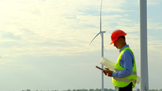 Wind driven generators produce power in field. Experienced engineer of maintenance checks operation of turbines via tablet at windmill station