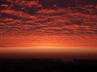 Red ominous clouds hovering above the ground at dawn. Red-tinted sky at sunrise. Landscape of tonal reds in the early hours