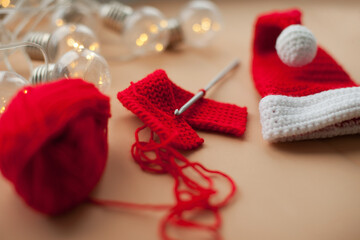 Crocheting a santa hat of red and white yarn on beige background for christmas gift