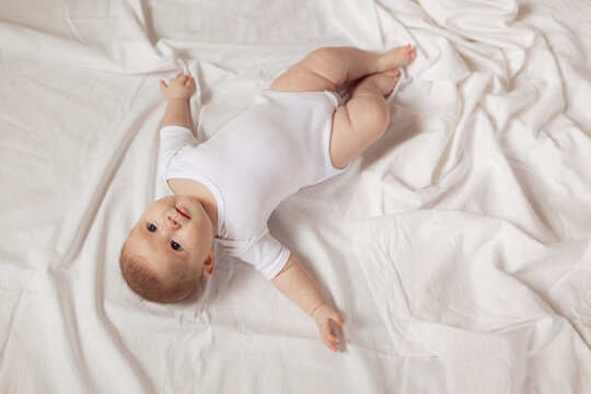 charming newborn baby in a white bodysuit lies on his back on a white fabric. top view. products for children. concept of happy childhood and motherhood. space for text. High quality photo