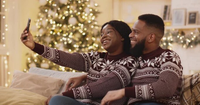 Christmas selfie. Young happy african american couple wearing winter sweaters making photo near Xmas tree at home