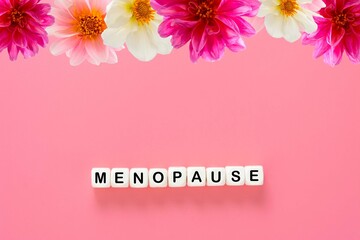 Menopause word abstract text, wooden blocks with dahlia flowers, over pink background