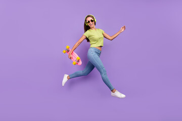 Fototapeta na wymiar Full length body size view of nice cheerful girl jumping listening hit having fun with skate isolated over purple violet color background
