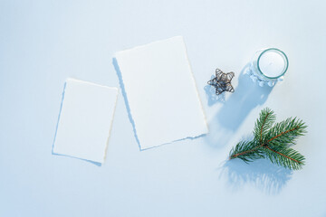Christmas blank greeting card mockup scene. Festive winter wedding composition.Candle, fir tree branch, Christmas decoration on white table.Cold light.Flat lay, top view
