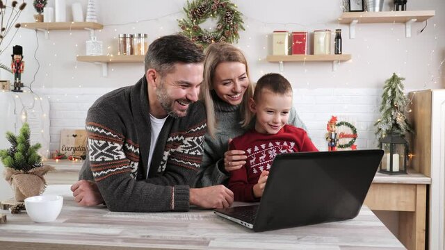 Couple in love with their male kid making online shopping in laptop enjoy winter Christmas New Year holidays at modern cozy house. Spend free time online, fun on internet, use new app on xmas Eve.