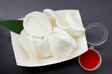 Junk food or fastfood concept. Rice chips on a black-white paper plate with sweet and sour or spicy chili sauce . Close-up of krupuk chips on black background. High quality photo