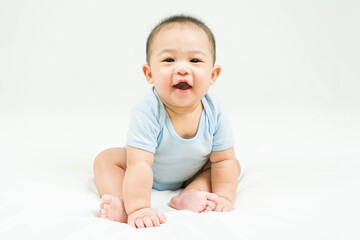 childhood and Childcare concept Portrait of cute little 5 months old  asian newborn baby boy wearing blue bodysuit sitting and smiling on white beedsheets.Selective focus.