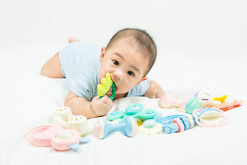 childhood and Childcare concept Portrait of cute little 5 months old  asian newborn baby boy wearing blue bodysuit having teeth growing issues teething pain while holding a bite toy lying on the bed.