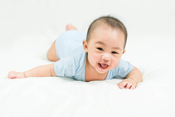 Childhood and Childcare concept Portrait of cute little 5 months old  asian newborn baby boy wearing blue bodysuit learn to crawl on white blanket at home.Smiling and looking camera.