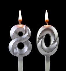 Burning silver birthday candle isolated on black background, number 80