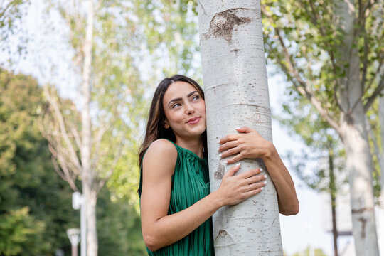 Smiling young woman hugging tree at park