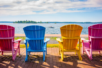 Four painted Adirondack chairs lined up along the bank of the St. Lawrence River in Clayton, New York.