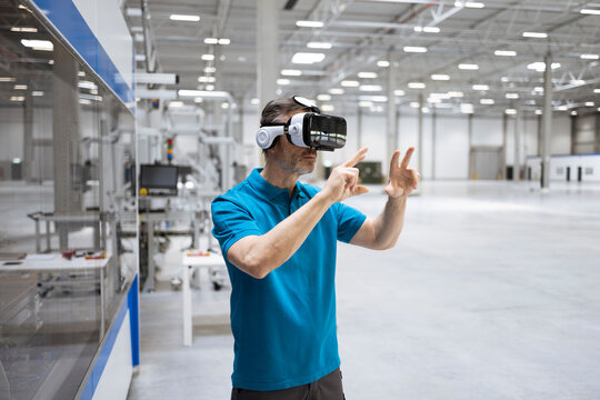 Male professional gesturing while using virtual reality headset in factory