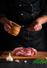 Cook sprinkles meat with salt. Preparing meat before baking. Working environment in the kitchen of a restaurant