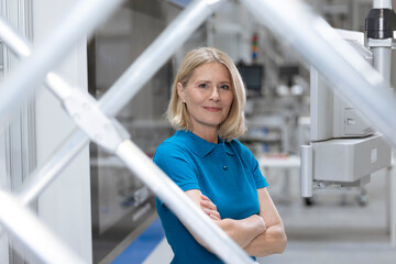 Smiling woman standing with arms crossed by machinery in factory