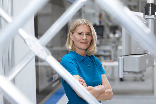 Smiling woman standing with arms crossed by machinery in factory