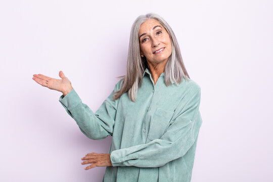 middle age gray hair woman smiling cheerfully, feeling happy and showing a concept in copy space with palm of hand