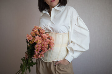 a girl in a white shirt and beige corset holds flowers in her hands