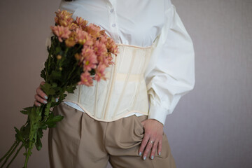 a girl in a white shirt and beige corset holds flowers in her hands