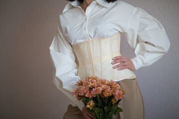 a girl in a white shirt and beige corset holds flowers in her hands