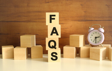 Four wooden cubes stacked vertically on a brown background form the word FAQS.