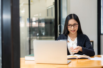 Serious woman sitting at a desk and working on laptop from home. Smiling Asian woman working, reading papers, report on successful female freelancer project. use a computer