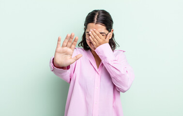 pretty teenager woman covering face with hand and putting other hand up front to stop camera,...