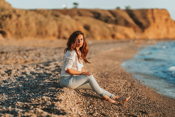 Fototapeta na wymiar A charming young woman in a white shirt and jeans on a calm romantic beach by the sea. Summer woman vacations concept. The concept of active life.