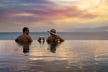 romantic getaways - couple drinking champagne and enjoying beautiful sunset in pool at tropical...