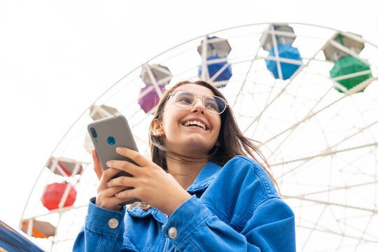 Positive woman using phone in city street under a ferris wheel