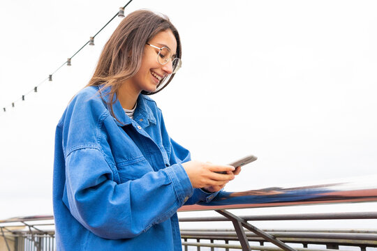 Positive woman using phone in city street near railing