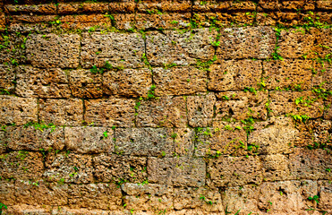 Stone masonry of walls and fences of ancient fortress structures covered with green moss. The ancient city of Angkor wat in Cambodia. Background wall with texture of green moss and plants.