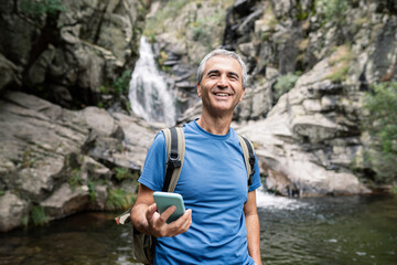 Smiling male tourist holding mobile phone in forest
