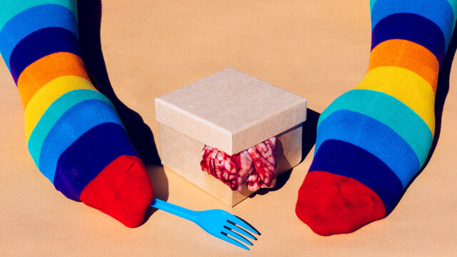 Unrecognizable person in multicolored socks on hands near carton box with brain
